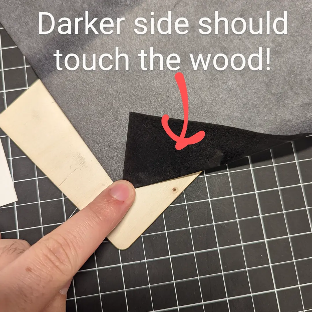 Image stating that it is important for the darker side of the carbon paper to be touching the wood.