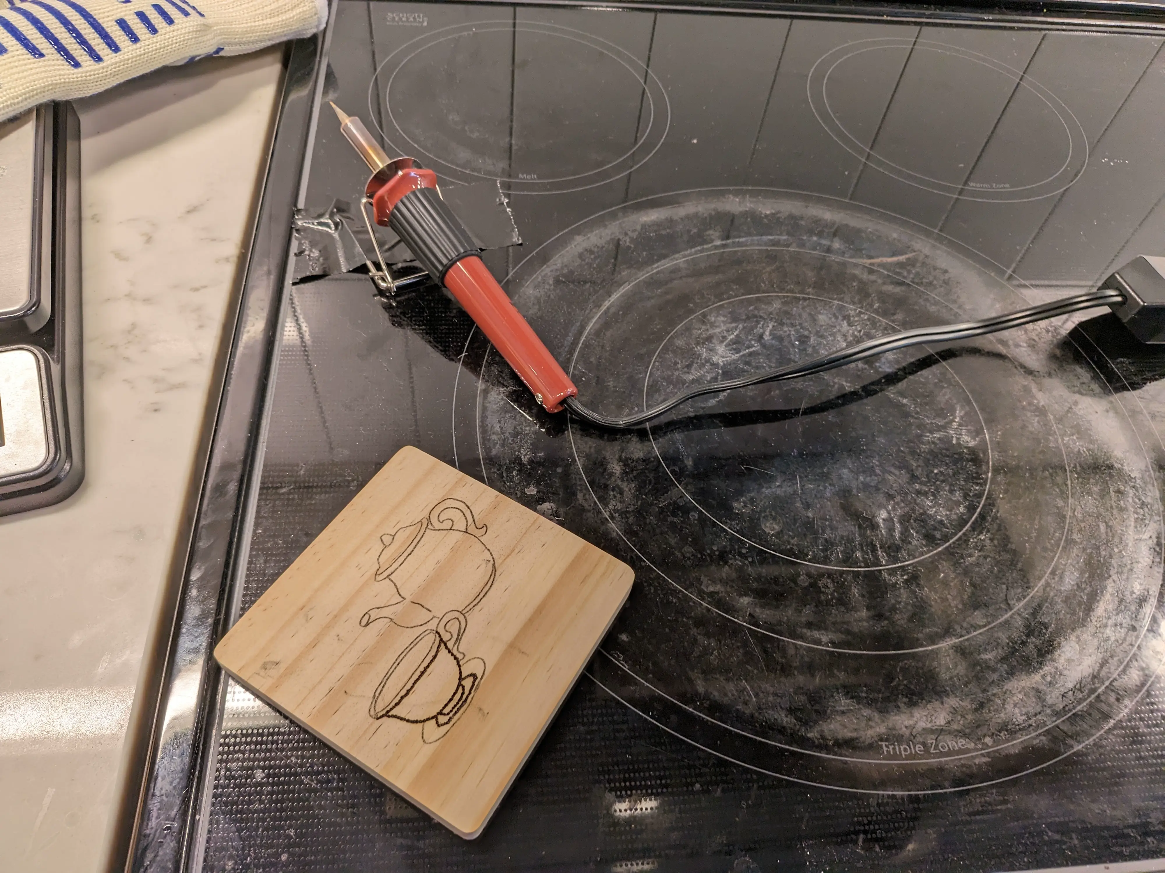 Image showing a wood burning tool resting on a stove being used like a table, with an in-progress coaster in the foreground.