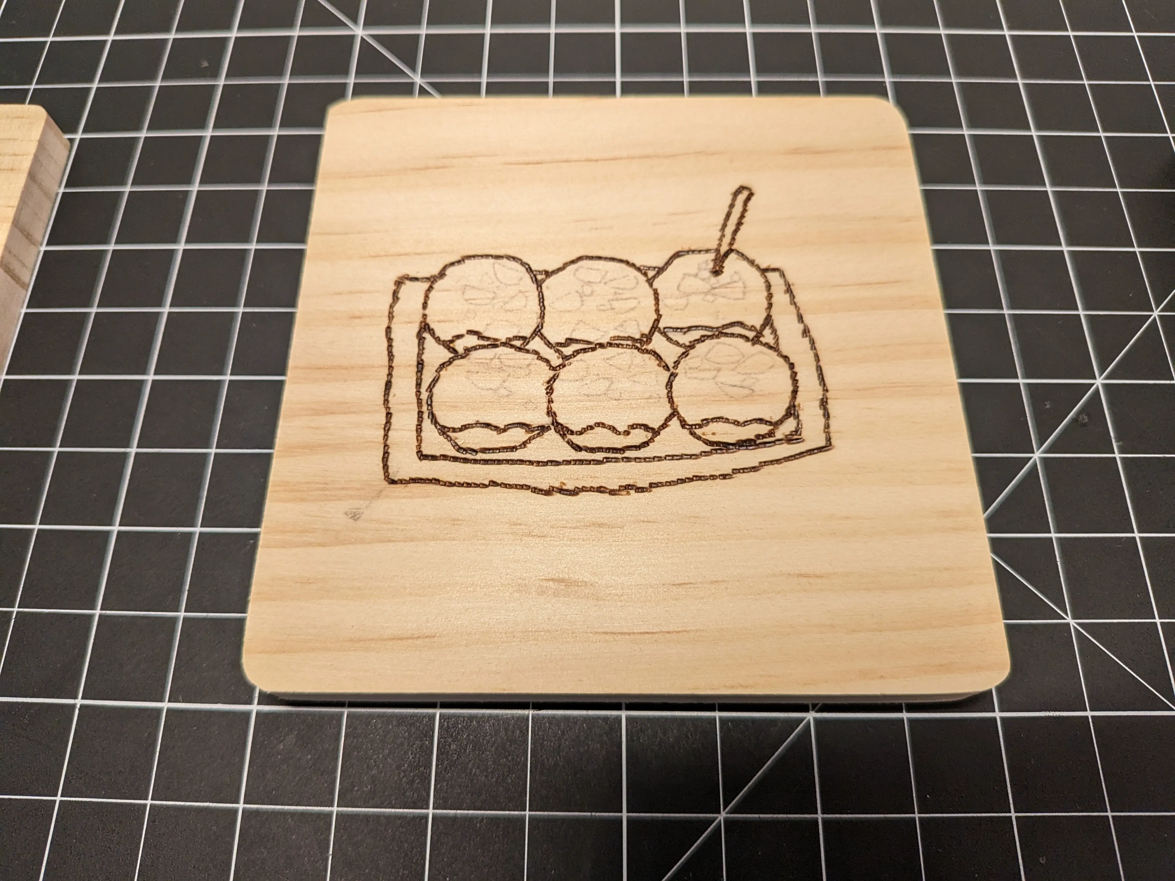 Image showing a wood burned coaster depicting takoyaki. Most of the lines are darkened (as they have been burned in) but you can see faint lines representing bonito flakes that were decided to not be burned in.